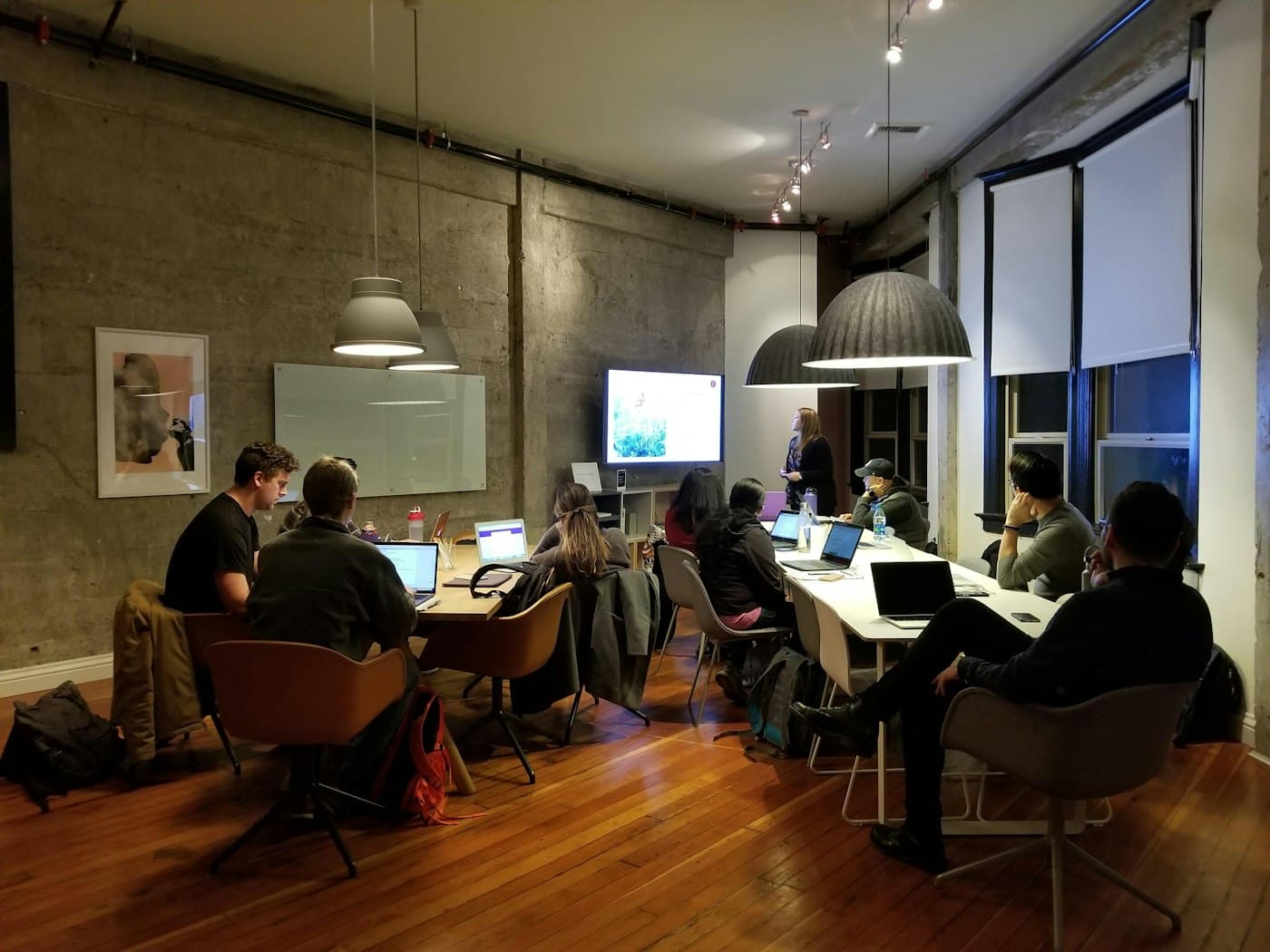 A team working on laptops around a long table in an evening workshop